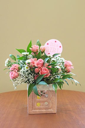 pink flowers in a pink and white container with the letter B on the front