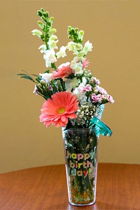 assorted flowers in a happy birthday drinking mug with a straw