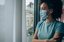 woman wearing a mask during covid looking worried while looking out a window